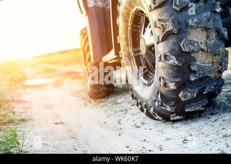 Close-up Schwanz Blick auf ATV Quad Bike auf Schmutz Land straße bei Sonnenuntergang am Abend Zeit. Dirty Rad der AWD All-terrain vehicle. Reisen und Abenteuer Konzept Stockfoto