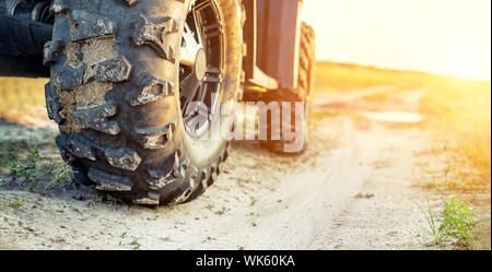 Close-up Schwanz Blick auf ATV Quad Bike auf Schmutz Land straße bei Sonnenuntergang am Abend Zeit. Dirty Rad der AWD All-terrain vehicle. Reisen und Abenteuer Konzept Stockfoto