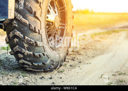 Close-up Schwanz Blick auf ATV Quad Bike auf Schmutz Land straße bei Sonnenuntergang am Abend Zeit. Dirty Rad der AWD All-terrain vehicle. Reisen und Abenteuer Konzept Stockfoto