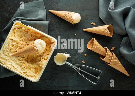 Vanilla Ice Cream scoops, Schaufelte aus Container in die waffle Kegel mit einem silbernen Utensil Stockfoto