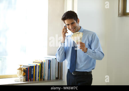 Geschäftsmann, der mit dem Mobiltelefon spricht und indische Banknoten in einem Büro hält Stockfoto