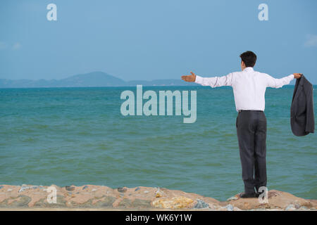 Rückansicht eines Geschäftsmanns, der mit ausgestrecktem Arm am Meer steht Stockfoto