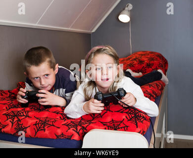 Geschwister spielen Videospiele lieing in das Bett Stockfoto