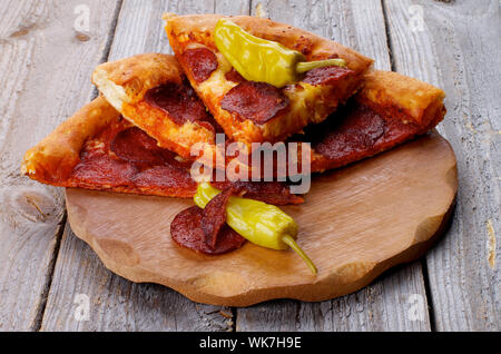 Stapel von leckere Pepperonipizza Scheiben mit zwei jalapeno Pfeffer auf Holzplatte closeup auf rustikalen Holzmöbeln Hintergrund Stockfoto