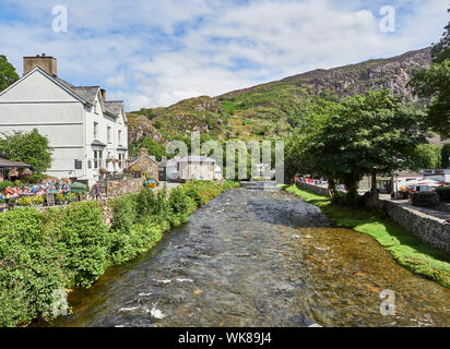 Blick auf den Fluss Glaslyn läuft durch das Dorf Beddgelert mit einem Haus und einer Straße entweder Seite an einem Sommertag Snowdonia, Gwynedd, Wales, Großbritannien Stockfoto