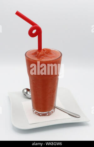 Hohes Glas Erdbeeren-Smoothie mit rotem Stroh, serviert auf einem weißen Teller mit Löffel, isoliert auf weißem Hintergrund Stockfoto