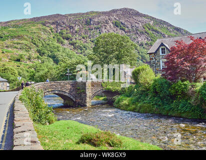 Blick auf eine Brücke aus Stein über den Fluss Glaslyn fließt durch die Stadt Beddgelert an einem Sommertag, Snowdonia, Gwynedd, Wales, Großbritannien Stockfoto