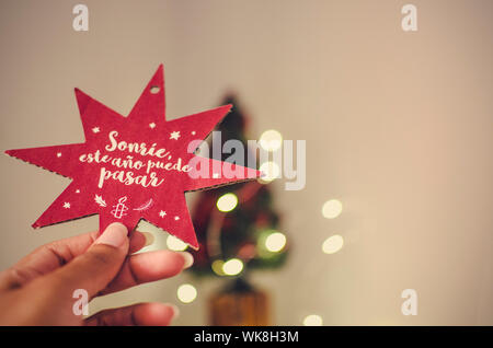 Hand eine schwarze Frau mit einem Weihnachtsstern mit einer Meldung in Spanisch (Lächeln, es in diesem Jahr passieren kann). Stockfoto
