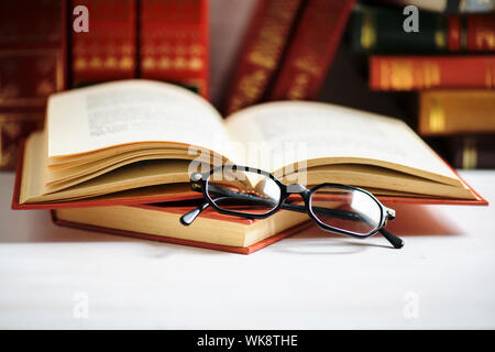 Stapel von Büchern mit schwarzen Gläsern auf das geöffnete Buch auf dem weißen Hintergrund mit Kopie Raum platziert Stockfoto