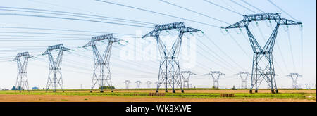 Panoramablick auf eine Reihe von Strommasten in der französischen Landschaft mit Dutzenden anderen Masten im Abstand unter einem klaren blauen Himmel. Stockfoto