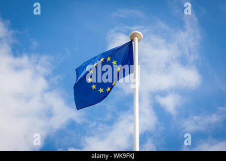 Die flatternde Fahne der Europäischen Union an einem Mast mit einem blauen Himmel mit weißen Wolken im Hintergrund Stockfoto