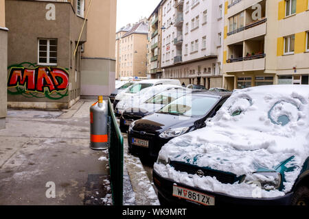 Lächelndes Gesicht mit Kulleraugen, die in den Schnee, auf ein Auto mit dem Wort Mad in Graffiti an der Wand geschrieben geschnitzt, auf einem Wiener Straße im Winter Stockfoto