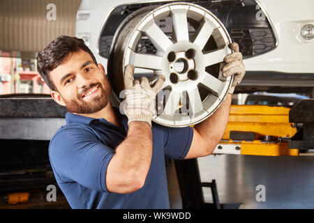 Junger Mann als Mechaniker Lehrling mit dem Auto Felge beim Wechsel von Rädern in der Kfz-werkstatt Stockfoto