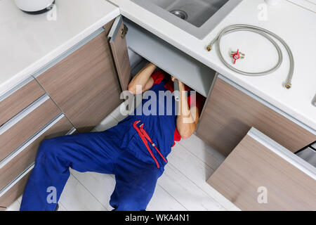 Klempner arbeiten unter heimischen Küche Spüle, Reparatur von Wasserleitungen Stockfoto
