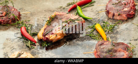 Panorama Banner der sortierten rohes Rindfleisch Steaks mit Filet Medaillons, Rinderfilet und T-Bone zusammen mit Kräutern und Chili peppers für Aromastoffe auf einer Tagung Stockfoto