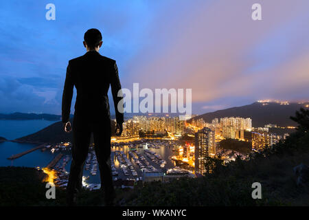 Asiatische Geschäftsmann stand auf dem Hügel und mit Blick auf die Wolkenkratzer und Hafen in Aberdeen, Hong Kong, Asien. Stockfoto