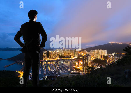 Asiatische Geschäftsmann stand auf dem Hügel und mit Blick auf die Wolkenkratzer und Hafen in Aberdeen, Hong Kong, Asien. Stockfoto