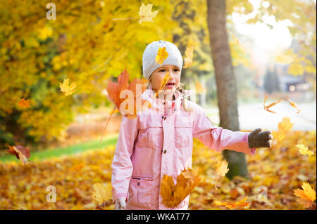 Süße kleine Mädchen mit fehlenden Zähne spielen mit gelbem Laub im Herbst Wald, trowing in die Luft. Glückliches Kind lachen und lächeln. Sonnig Stockfoto