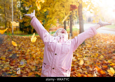 Süße kleine Mädchen mit fehlenden Zähne spielen mit gelbem Laub im Herbst Wald, trowing in die Luft. Glückliches Kind lachen und lächeln. Sonnig Stockfoto