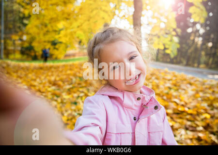 Süße kleine Mädchen mit fehlenden Zähne unter selfie. Glückliches Kind lachen und lächeln. Sonnige Herbst Wald, Sun Beam. Stockfoto