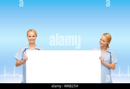 Gesundheitswesen, Medizin, Werbung und Verkauf Konzept - lächelnd weibliche Ärzte oder Krankenschwestern mit Stethoskop und weiße leere Brett Stockfoto