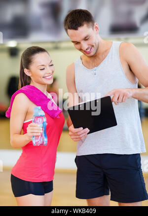 Fitness, Sport, Training, Fitness und Lifestyle Konzept - lächelnd männlichen Trainer mit Zwischenablage und Frau mit Wasserflasche in der Turnhalle Stockfoto