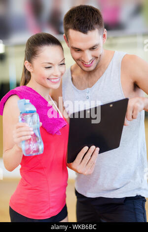 Fitness, Sport, Training, Fitness und Lifestyle Konzept - lächelnd männlichen Trainer mit Zwischenablage und Frau mit Wasserflasche in der Turnhalle Stockfoto