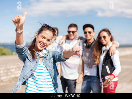 Sommerferien und Teenage Konzept-Jugendmädchen in Sonnenbrille und Kopfhörer mit Freunden außerhalb und Daumen hoch Stockfoto