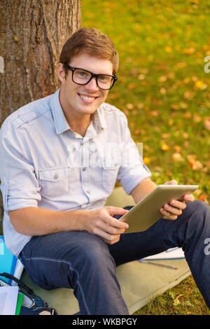 Bildung, Technologie und Internet Konzept - Lächeln männlicher Student in Brillen mit tablet pc außerhalb Stockfoto