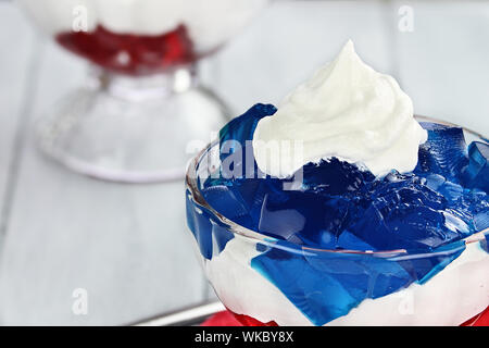 Gelatine 2-in-1-Dessert von kuben von roten und blauen Wackelpudding mit weißen flauschigen Schlagsahne für den vierten Juli Urlaub. Geringe Tiefenschärfe. Stockfoto