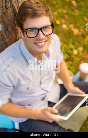 Bildung, Technologie und Internet Konzept - Lächeln männlicher Student in Brillen mit tablet pc außerhalb Stockfoto