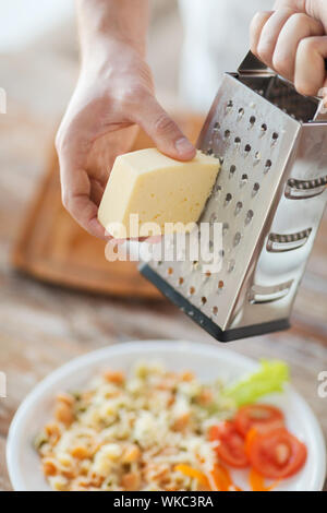 Nahaufnahme von männlichen Händen reiben von Käse über Nudeln Stockfoto