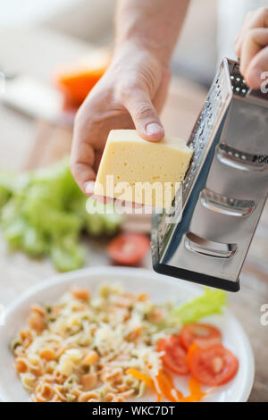 Nahaufnahme von männlichen Händen reiben von Käse über Nudeln Stockfoto