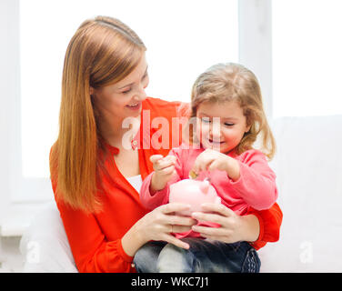 Familie, Kinder, Geld, Investment und glückliche Menschen Konzept - glückliche Mutter und Tochter mit kleinen rosa Sparschwein Stockfoto