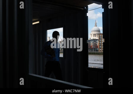Ein Mann Spaziergänge entlang der Uferstraße entlang der Themse in London, St Paul's Kathedrale im Hintergrund. Stockfoto