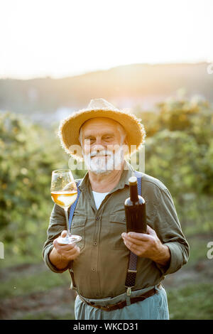 Portrait eines älteren gut gekleideten Winzer Kontrolle der Wein Qualität im Weinberg bei einem Sonnenuntergang. Konzept der Weinbereitung im Alter Stockfoto