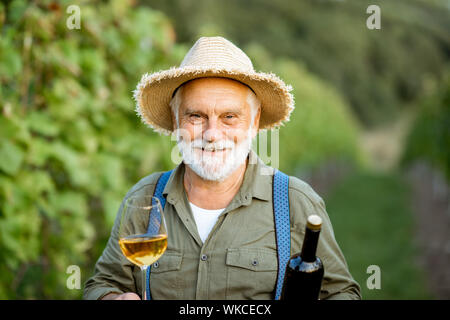 Portrait Of Happy senior gut gekleideten Winzer Wein Qualität prüfen, stehend mit Wein Glas und Flasche auf dem Weinberg Stockfoto