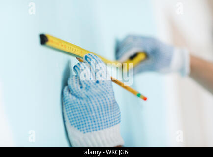 Reparatur-, Gebäude- und Home Konzept - Nahaufnahme der männlichen in Handschuhe messen mit Klebeband an der Wand Stockfoto