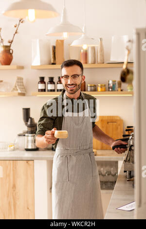 Begrüßung der Gäste. Fröhliche stattlichen Barista tragen gestreifte Schürze Begrüßung der Gäste und Kaffee Stockfoto