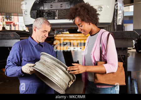 Automechaniker zeigt Kunden ein kaputtes Auto Felge während der Inspektion in der Werkstatt Stockfoto