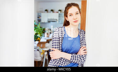 Junge Frau lehnt sich an die Tür in der neuen Wohnung nach dem Umzug Stockfoto