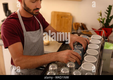 Stattliche Barista. Stattliche barista tragen gestreifte Schürze, cups auf Kaffeemaschine Stockfoto