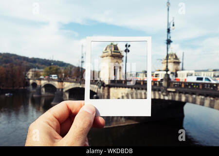 Nahaufnahme eines jungen kaukasischen Mann mit einem weißen Rahmen in seiner Hand, das Framing der Legionen Brücke über der Moldau in Prag, Tschechische Republik, simulati Stockfoto