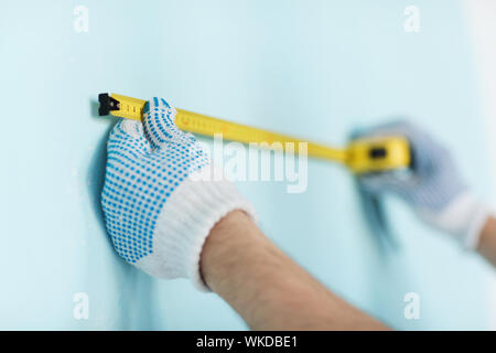 Reparatur-, Gebäude- und Home Konzept - Nahaufnahme der männlichen in Handschuhe messen mit Klebeband an der Wand Stockfoto