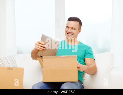 Post nach Hause, Technologie und Lifestyle-Konzept - lächelnd Mann Eröffnung Karton mit Tablet-pc-Computer drin Stockfoto