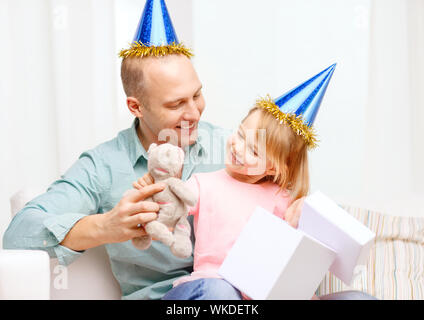 Familie, Kinder, Feier, Urlaub, Geburtstag und glückliche Menschen Konzept - glücklicher Vater und Tochter in blauen Partyhüte mit Geschenk-box Stockfoto