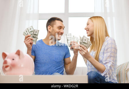 Liebe, Familie, Finanzen, Geld und Glück Concpet - paar mit Geld und Sparschwein ot Tisch daheim lächelnd Stockfoto
