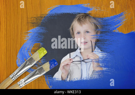 Das zusammengesetzte Bild des kleinen Jungen in der Schule gegen Holz Kiefer Tisch mit Pinsel Stockfoto