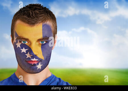 Das zusammengesetzte Bild von Bosnien Fußball-Fan im Gesicht Farbe gegen Fußballplatz unter blauem Himmel Stockfoto