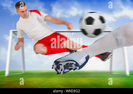 Das zusammengesetzte Bild von Fußballspielern Bekämpfung für den Ball gegen Fußballplatz und Ziel unter blauem Himmel Stockfoto